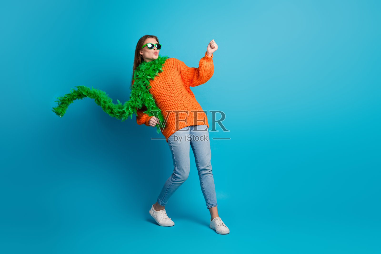 身穿时尚橙色毛衣的美丽年轻女子，在充满活力的蓝色背景前，挥舞着围巾，尽情舞动，玩得开心照片摄影图片