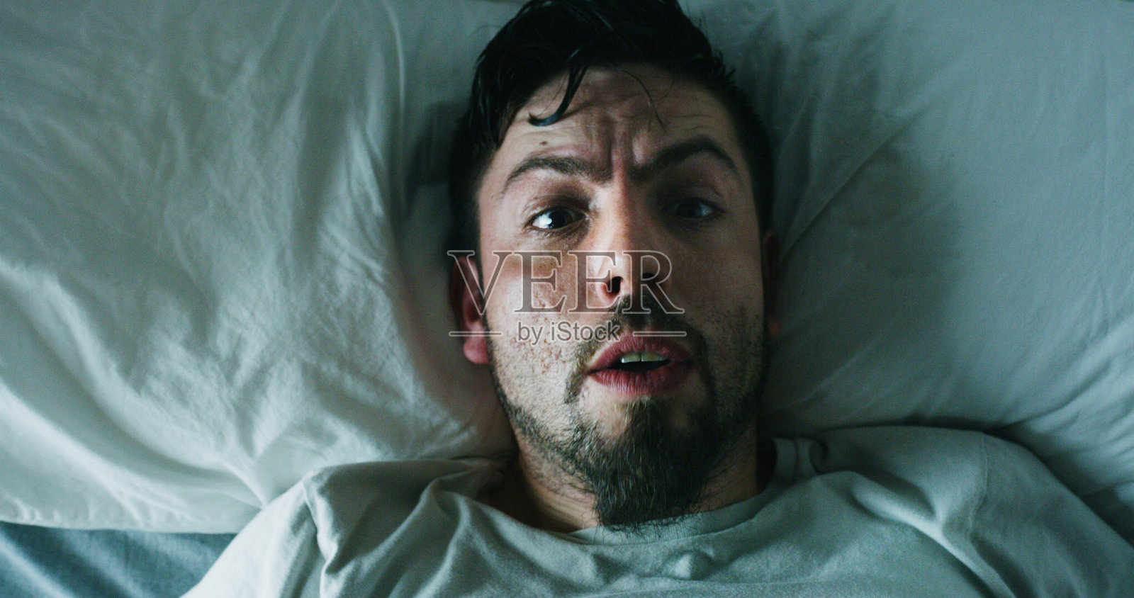 男人肖像，床上方是表现精神错乱、心理健康或失眠在精神病院的噩梦。俯视视角，男性人物或清醒状态，带着惊吓、恐慌或恐惧，表现偏执压力或睡眠呼吸暂停在卧室。照片摄影图片