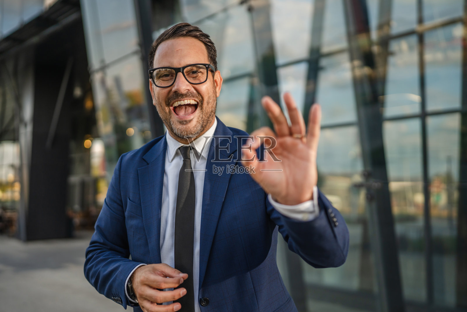 微笑着的商人坐在办公楼前，打出“OK”手势。照片摄影图片