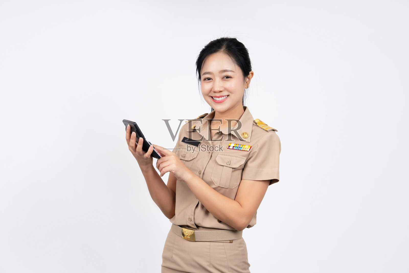 一名身穿棕色泰国政府制服的快乐亚洲女性，在白色背景上拿着一个独立的计算器。金融概念。照片摄影图片