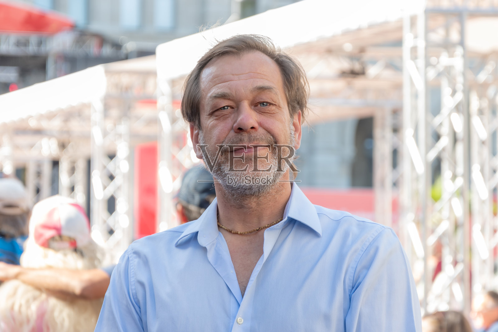 一位50-55岁的男子穿着蓝色衬衫，面带笑容，背景是熙熙攘攘的城市人群。照片摄影图片