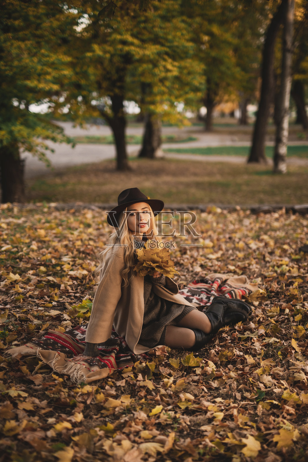 一位女士在阳光明媚的秋日，身着时尚的帽子和外套在户外散步。照片摄影图片