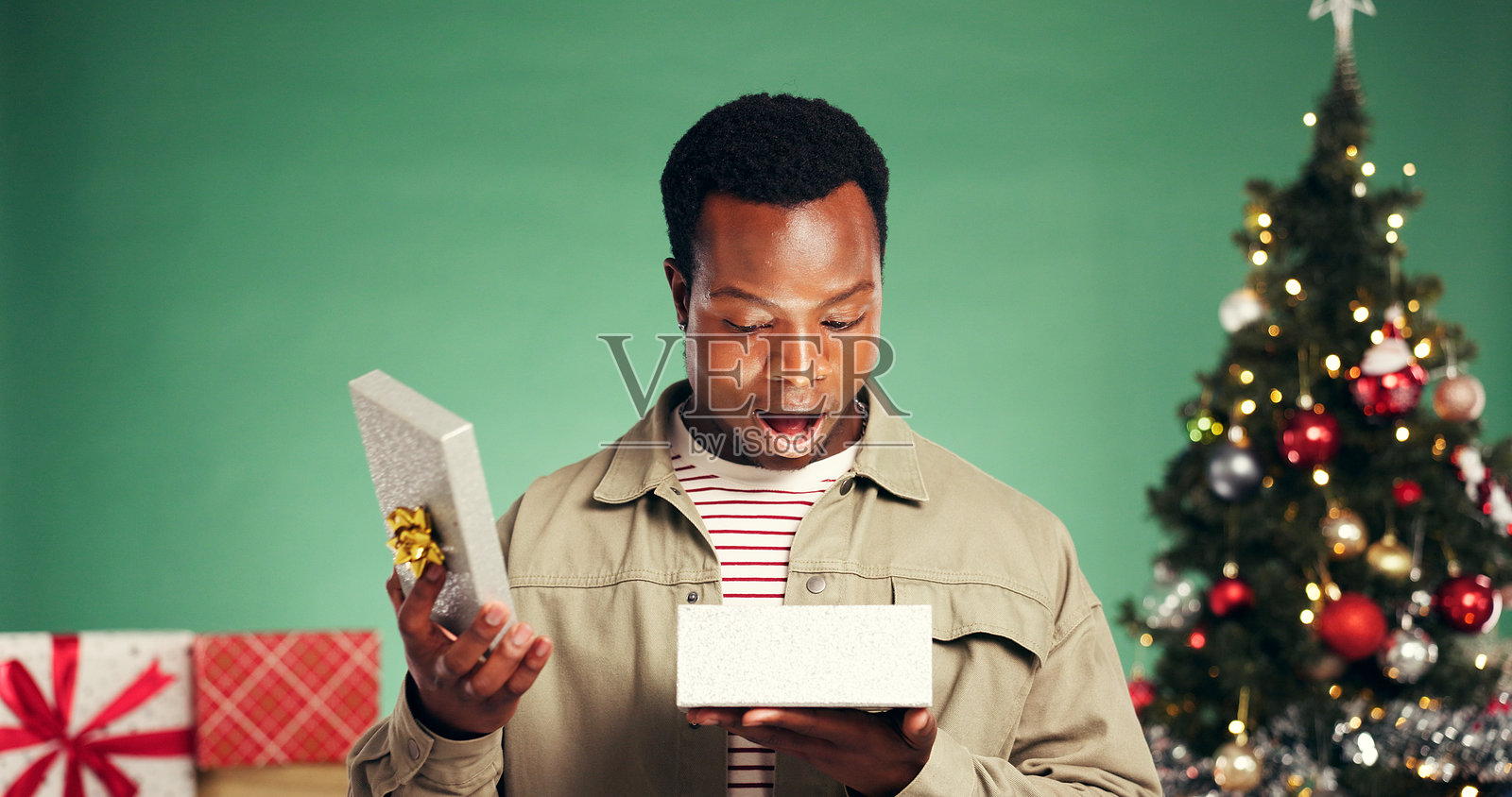 圣诞节，黑人男子在工作室里收到了节日的礼物和惊喜，这是假期、庆祝和圣诞包裹的时刻。他在绿色背景前收到了一个令人惊叹的礼物盒子，看起来非常惊喜，嘴巴张开，表示“哇”和“我的天”。照片摄影图片