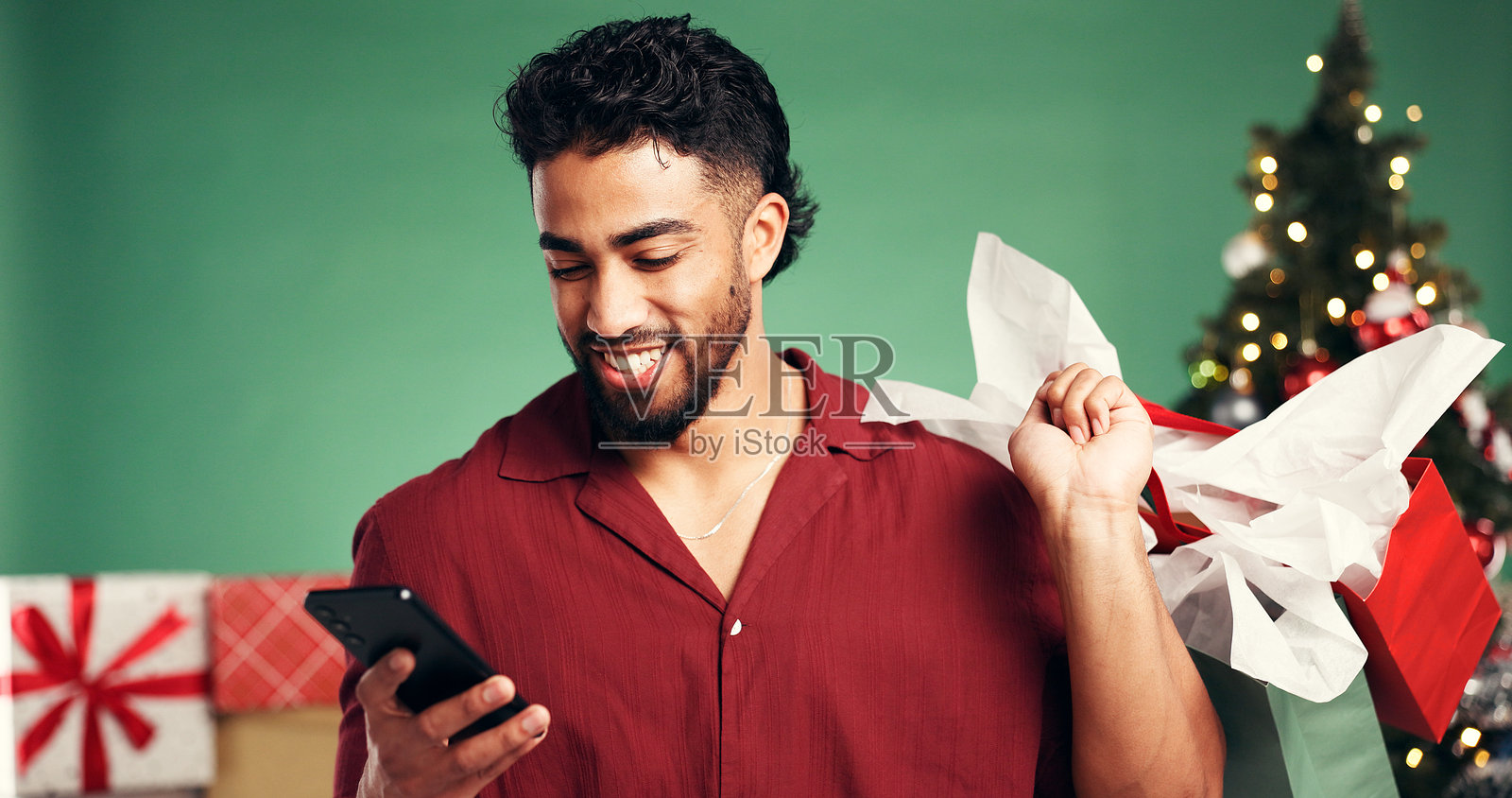 购物袋、圣诞节和使用智能手机的男人，适用于工作室或折扣，可在十二月节日期间作为礼物。电子商务、购物和拥有礼物的个人，适用于圣诞节，绿色背景，并在手机应用上浏览。照片摄影图片