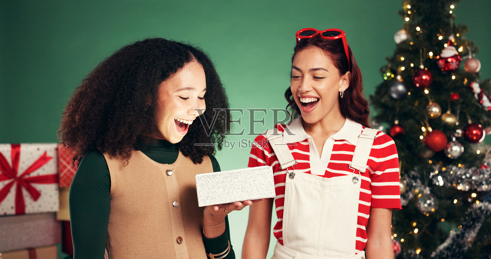 圣诞节，朋友们在影棚里为节日季准备的礼物和惊喜，充满庆祝气氛的圣诞包裹。一位女士提着盒子，面带微笑，背景为绿色，象征着节日传统、人与人之间的联结以及惊喜。照片摄影图片