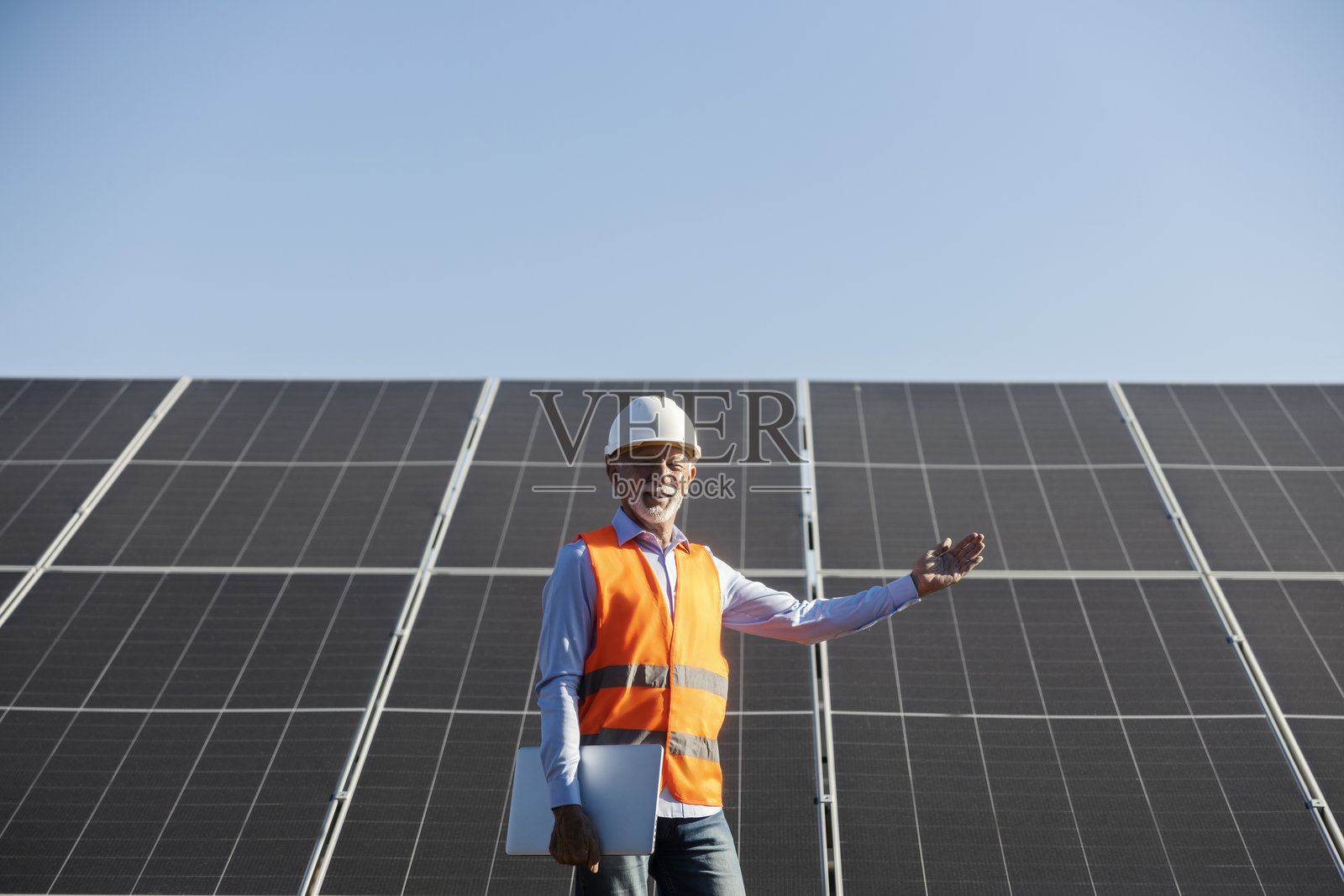 夕阳下，身穿防护装备的年长男性工人在检查太阳能电池板。照片摄影图片