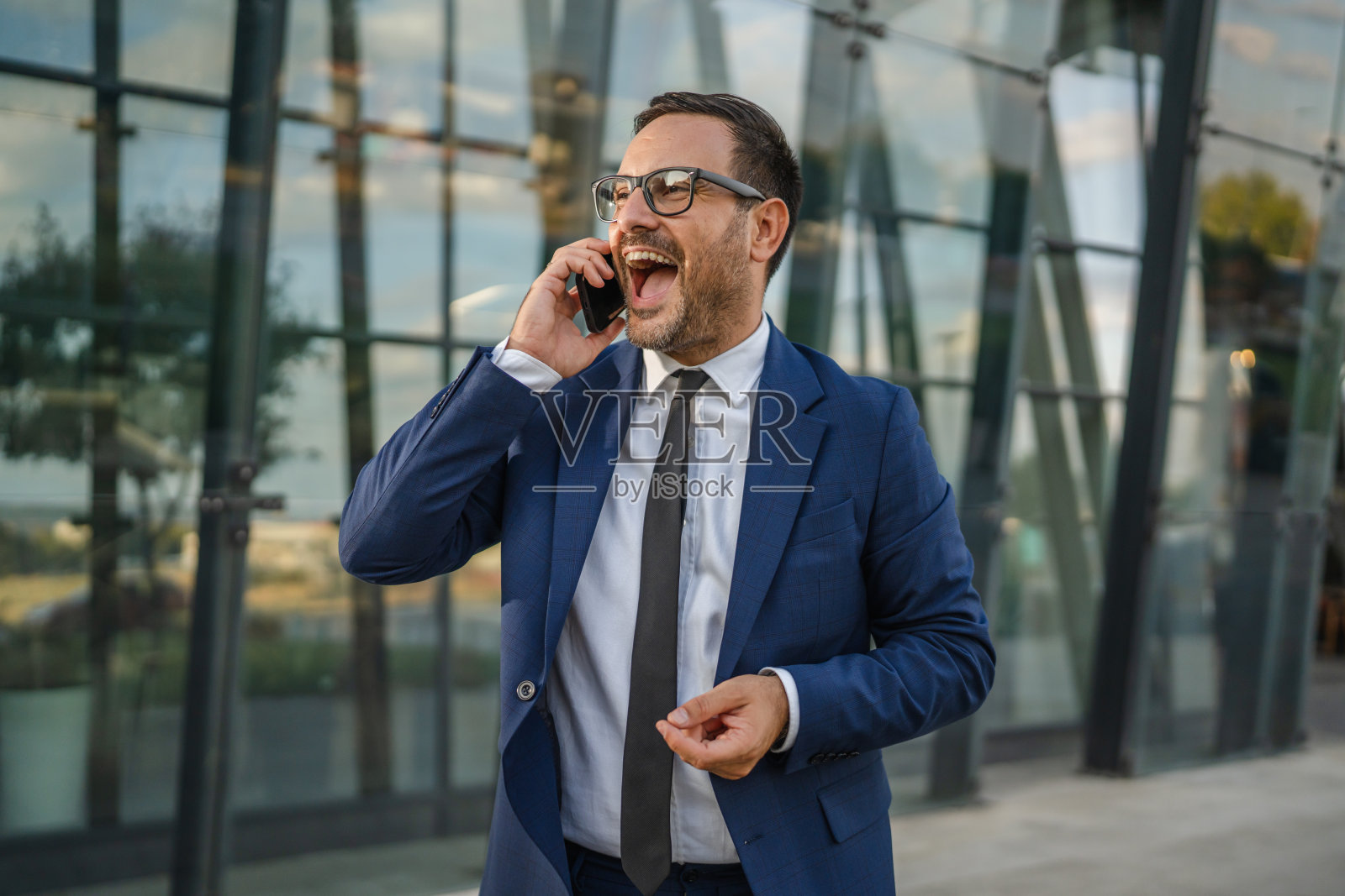 商务人士在办公楼外打电话，脸上洋溢着兴奋和热情。照片摄影图片