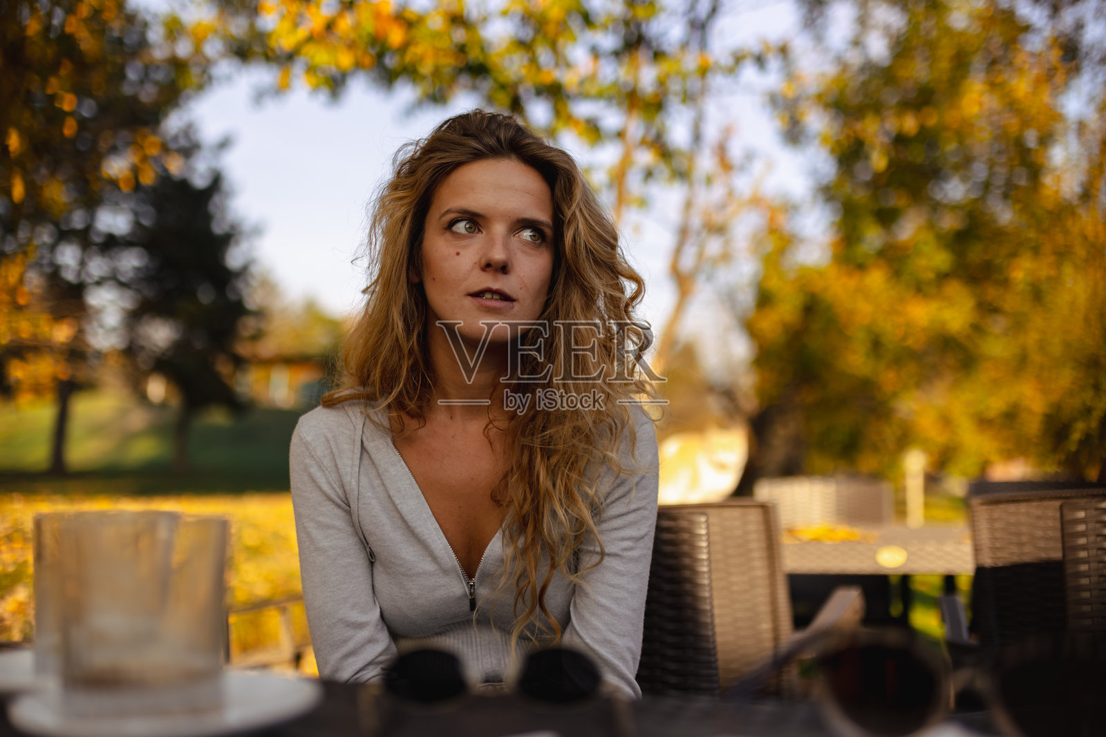 一位年轻女子，留着卷发，秋季时坐在户外，周围环绕着五彩斑斓的落叶，在宁静的咖啡馆环境中享受着安详的时光。照片摄影图片