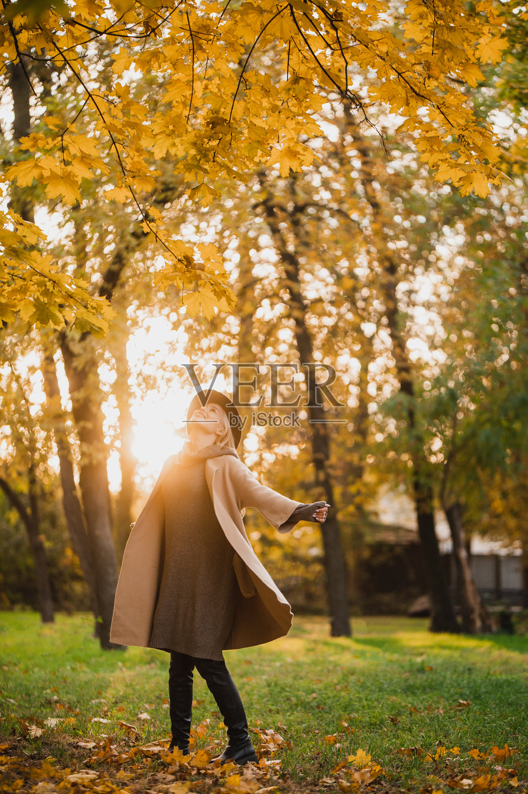 阳光明媚的秋日，一位女士戴着时尚的帽子、穿着外套在户外散步。照片摄影图片