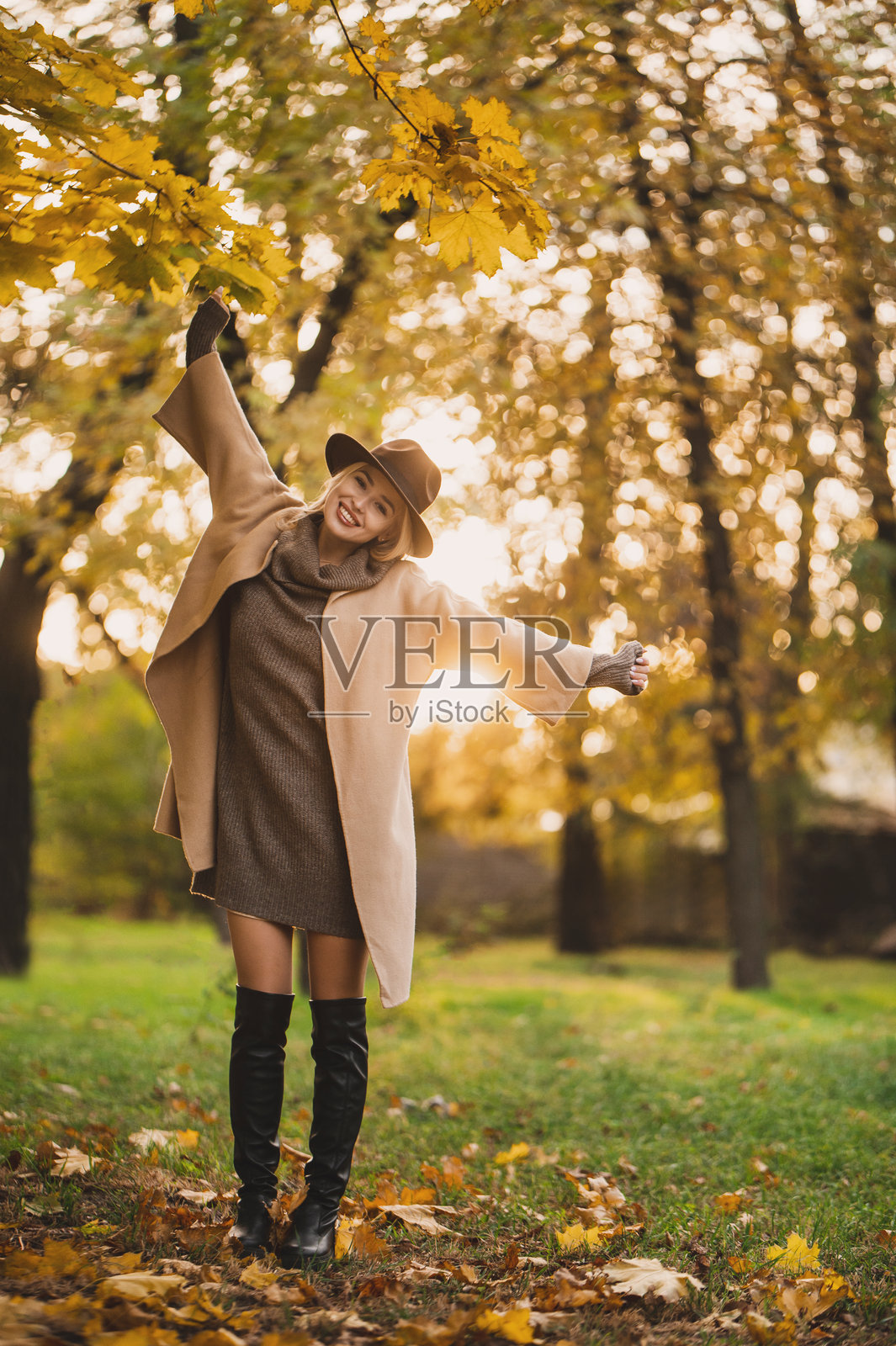 一位女士在阳光明媚的秋日，戴着时尚的帽子，穿着外套在户外散步。照片摄影图片