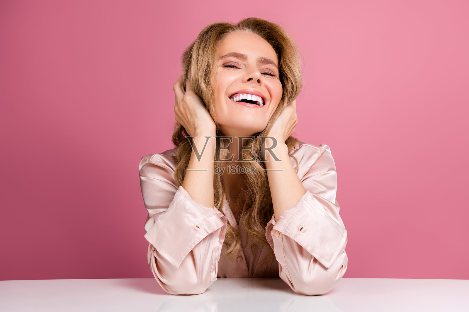 粉色睡衣的成成熟的女人士自信地摆出姿势，背景是柔和的粉色，体现出美丽与魅力。照片摄影图片