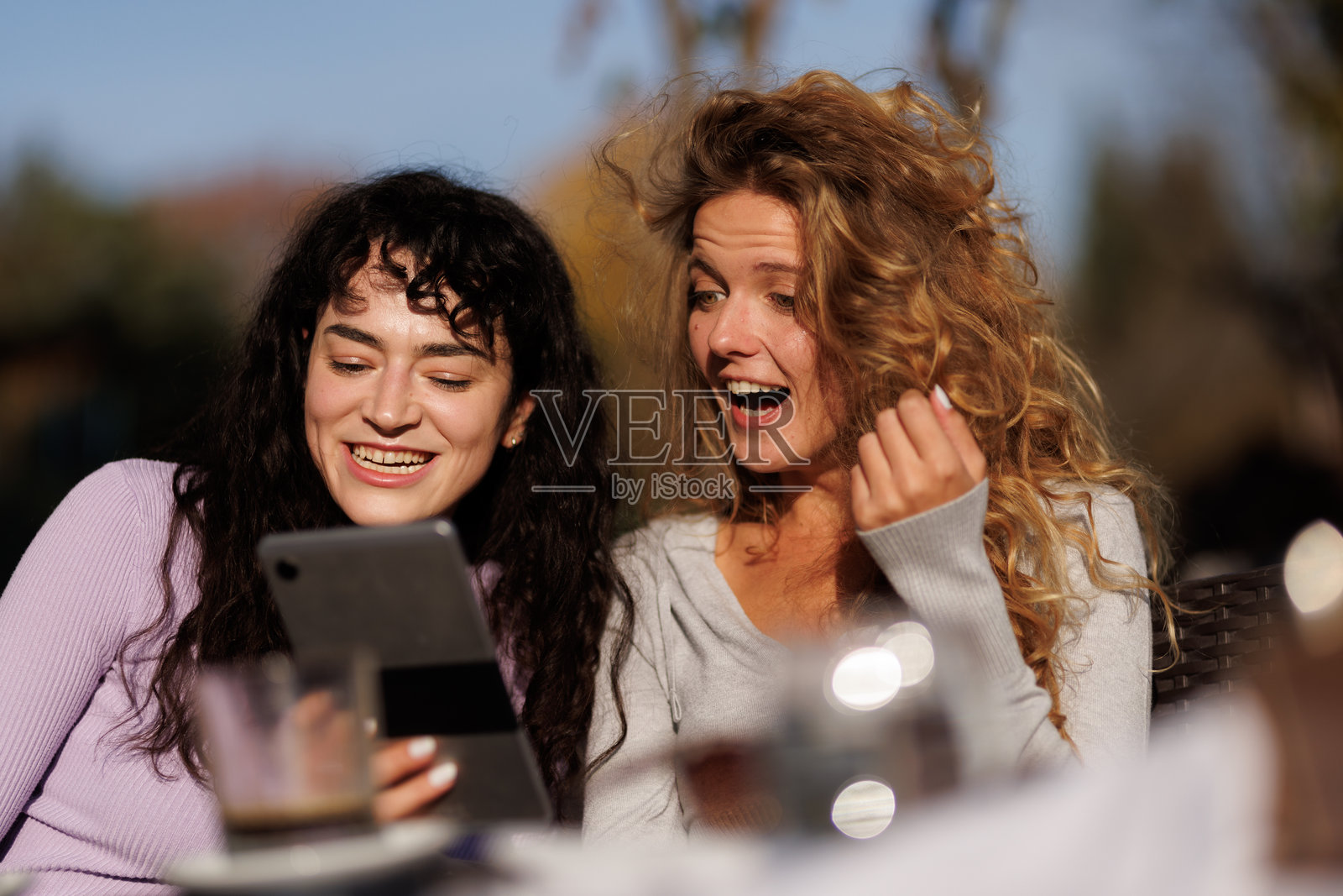 朋友们在户外的咖啡馆享受阳光明媚的一天，一起使用平板电脑分享欢乐的时光和笑声。照片摄影图片