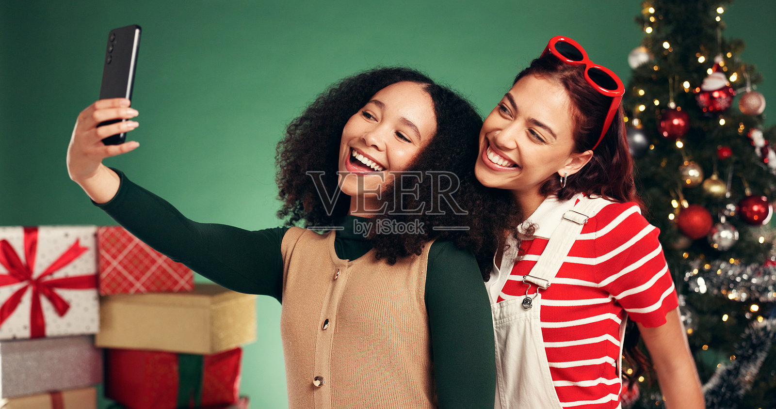 女性、朋友们在圣诞节自拍，在十二月假期的工作室里留下回忆，享受节日带来的亲密时光。绿色背景，人们在圣诞季感到兴奋，拍摄快乐的个人资料照片用于社交媒体帖子。照片摄影图片