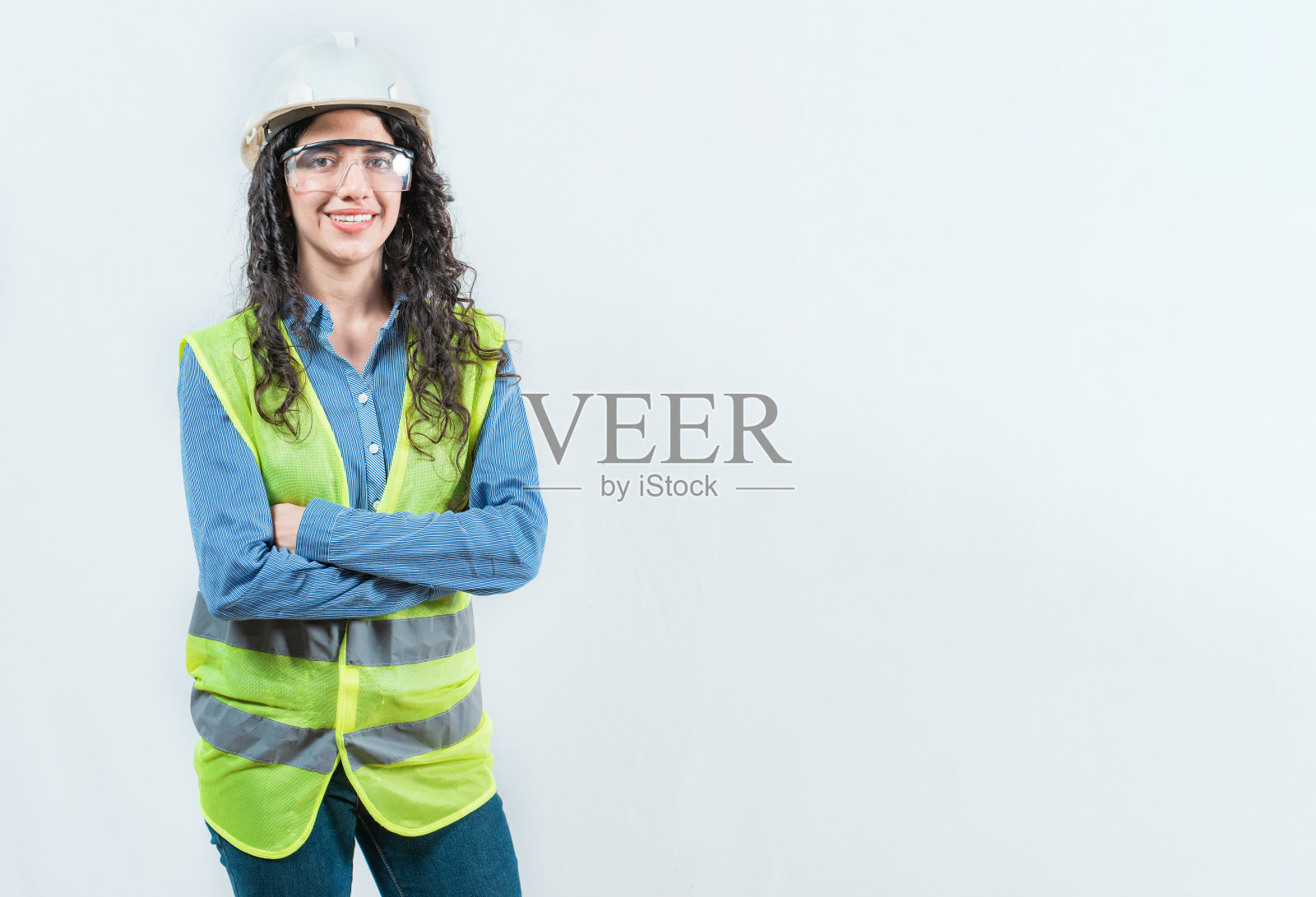 一位戴着头盔和背心的年轻女工程师，面带微笑，双臂交叉，正面看向镜头，背景为纯色隔离。照片摄影图片