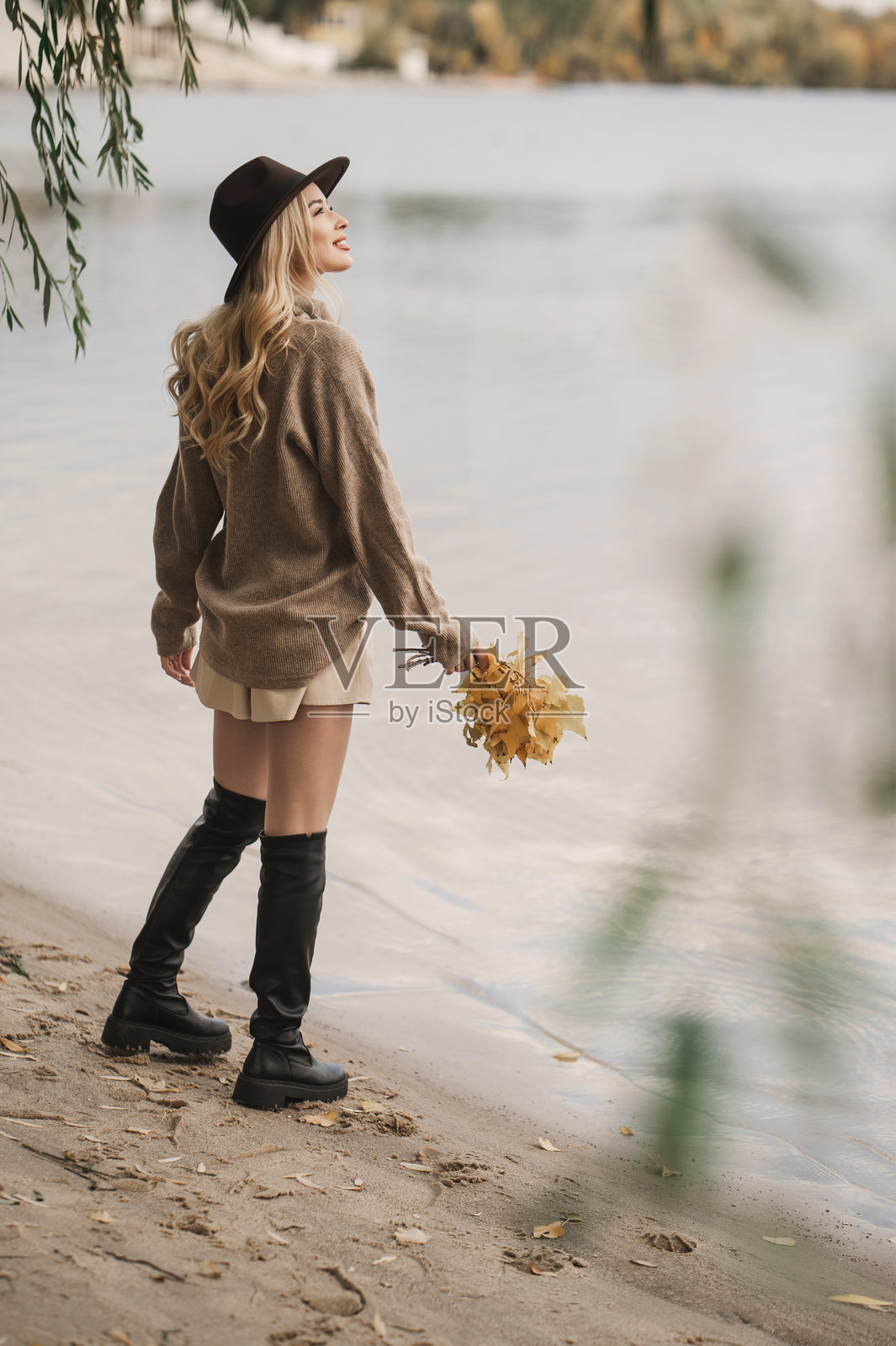 秋日暖阳，一位女士头戴时髦的帽子，身穿外套，在户外悠闲漫步。照片摄影图片