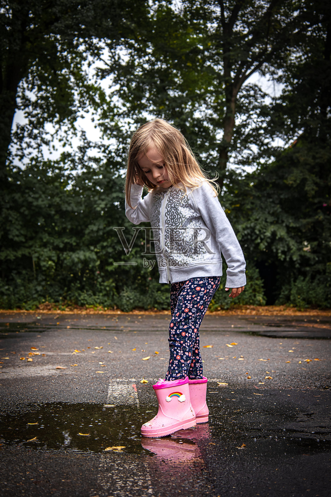 穿着粉色靴子的小女孩在水坑边照片摄影图片
