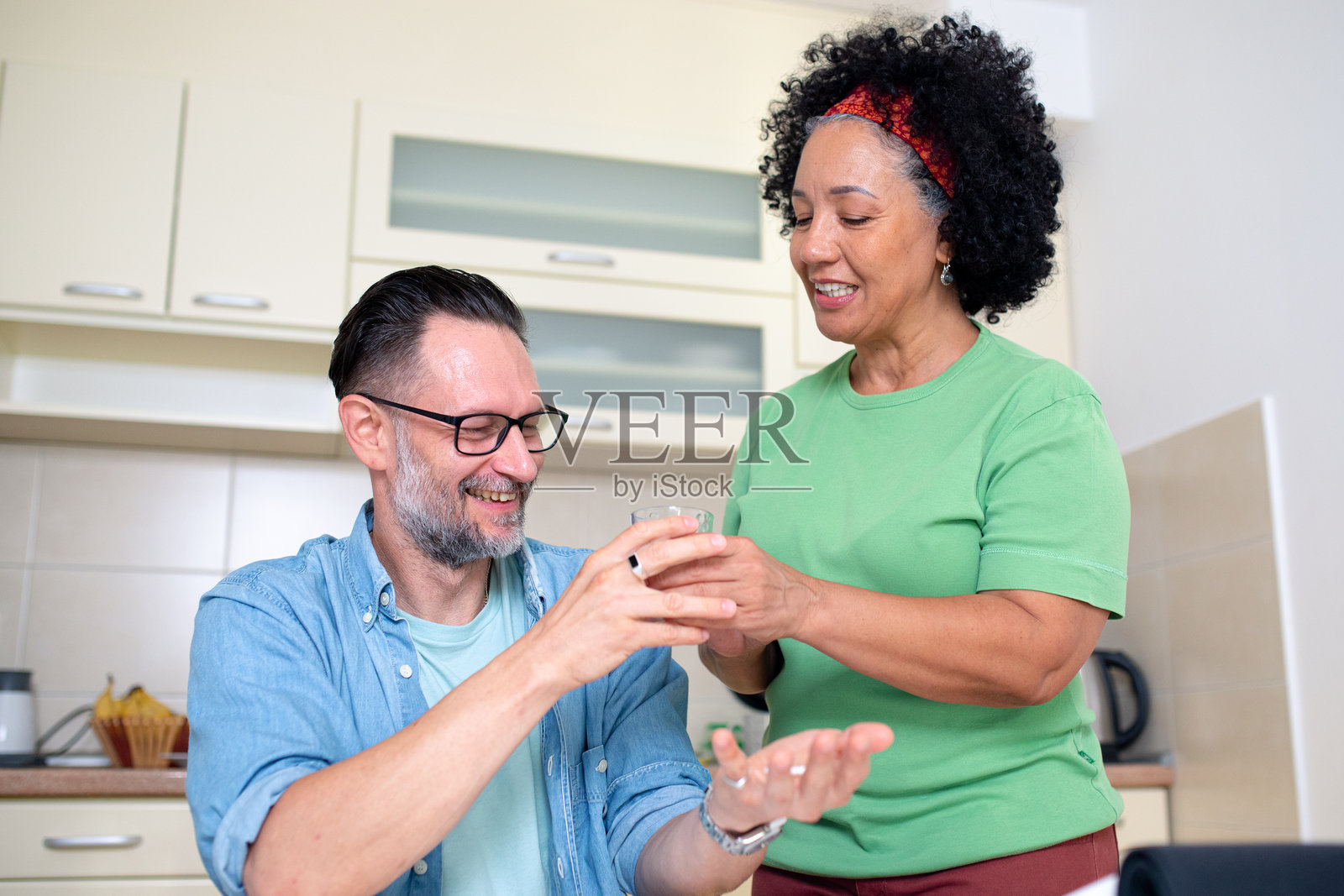 女人在厨房给微笑着的男人喂药和水照片摄影图片