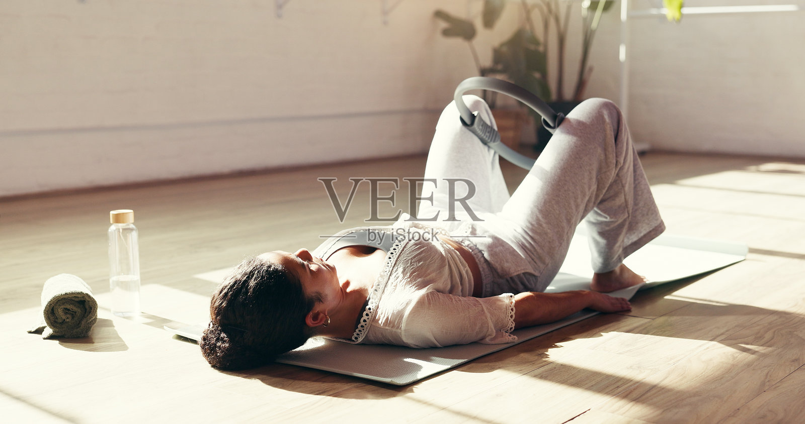 一名女性在瑜伽垫上使用普拉提环进行锻炼，以增强力量、锻炼臀部肌肉、提升身体平衡和核心稳定性，促进健康。照片摄影图片