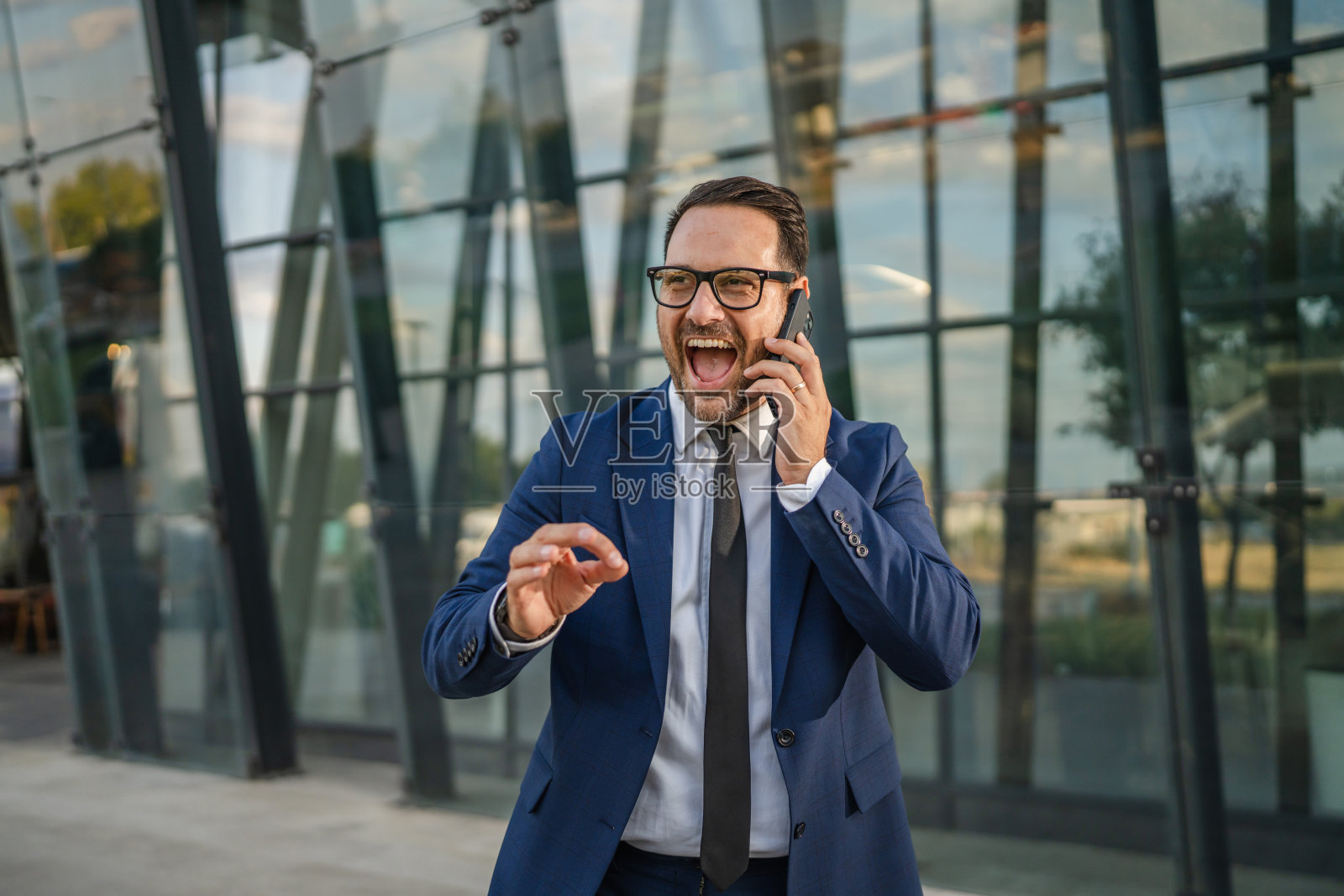 一位商务人士在办公楼外讲电话，显得兴奋而热情。照片摄影图片