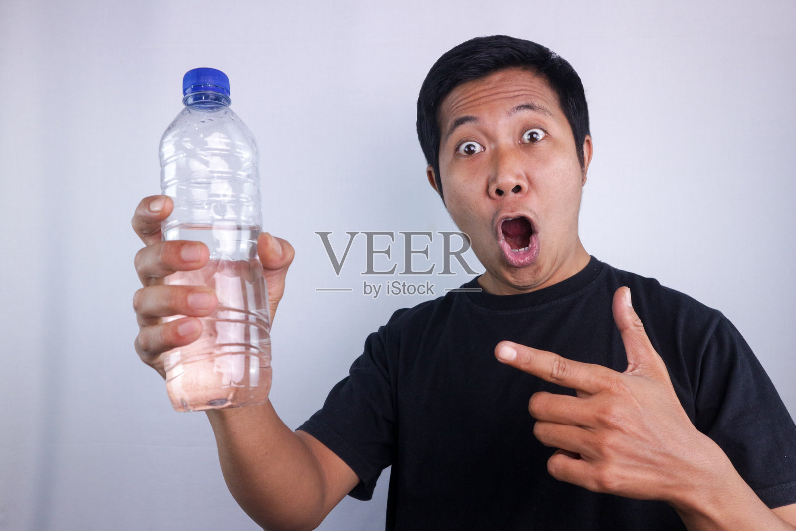 亚洲男性兴奋地用手指着矿泉水瓶，瓶子是孤立在白色的背景上。照片摄影图片