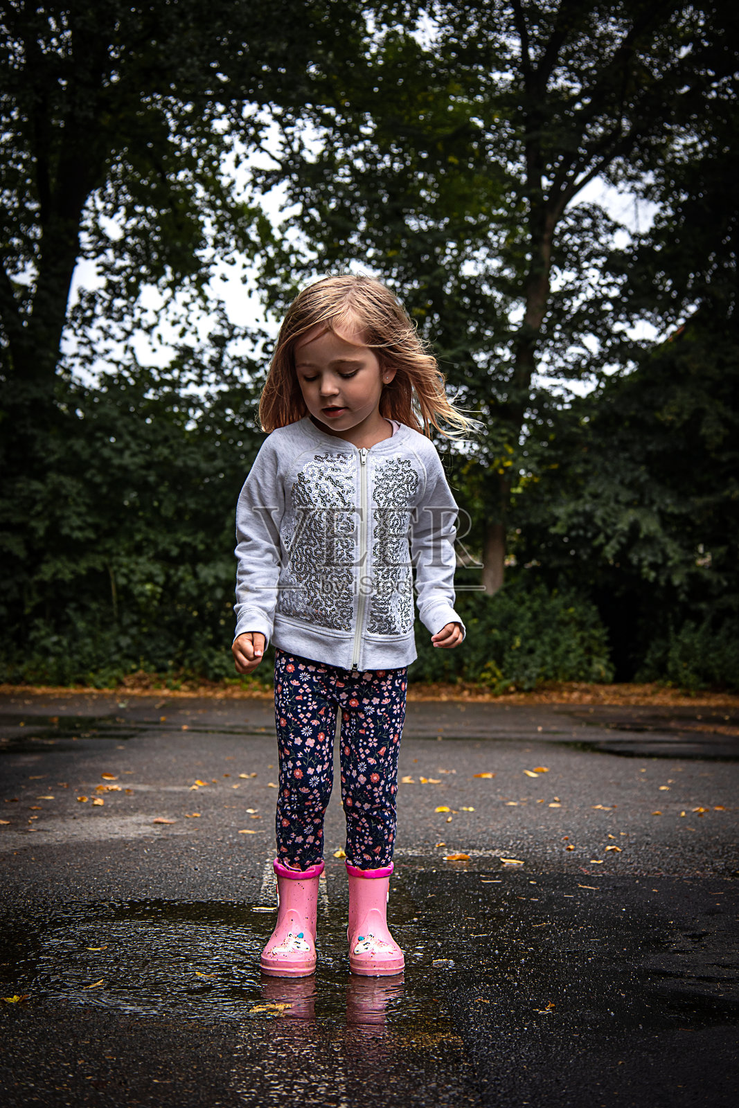 可爱的小女孩在沥青路上的水坑里跳跃照片摄影图片