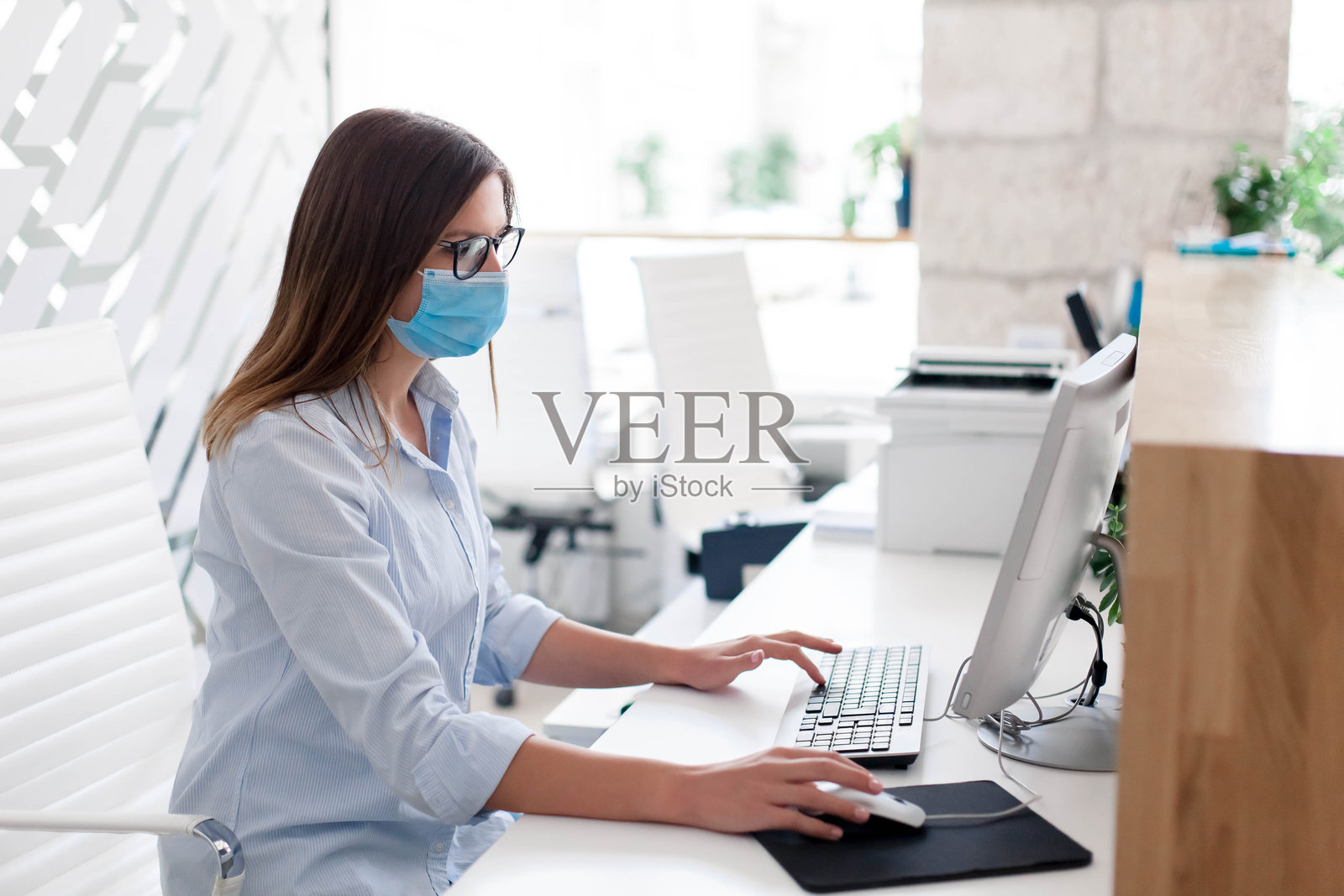 年轻女子在办公室戴着医用口罩。保护工作场所的员工。女孩在工作。照片摄影图片