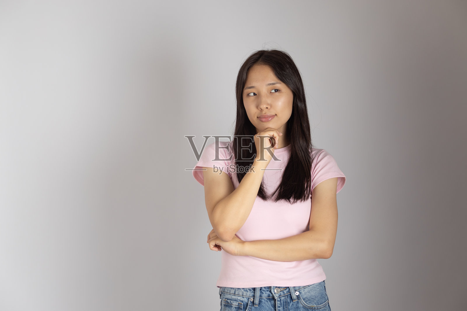 一个留着深色长发的年轻亚洲女性，站在纯色的浅色背景前。照片摄影图片