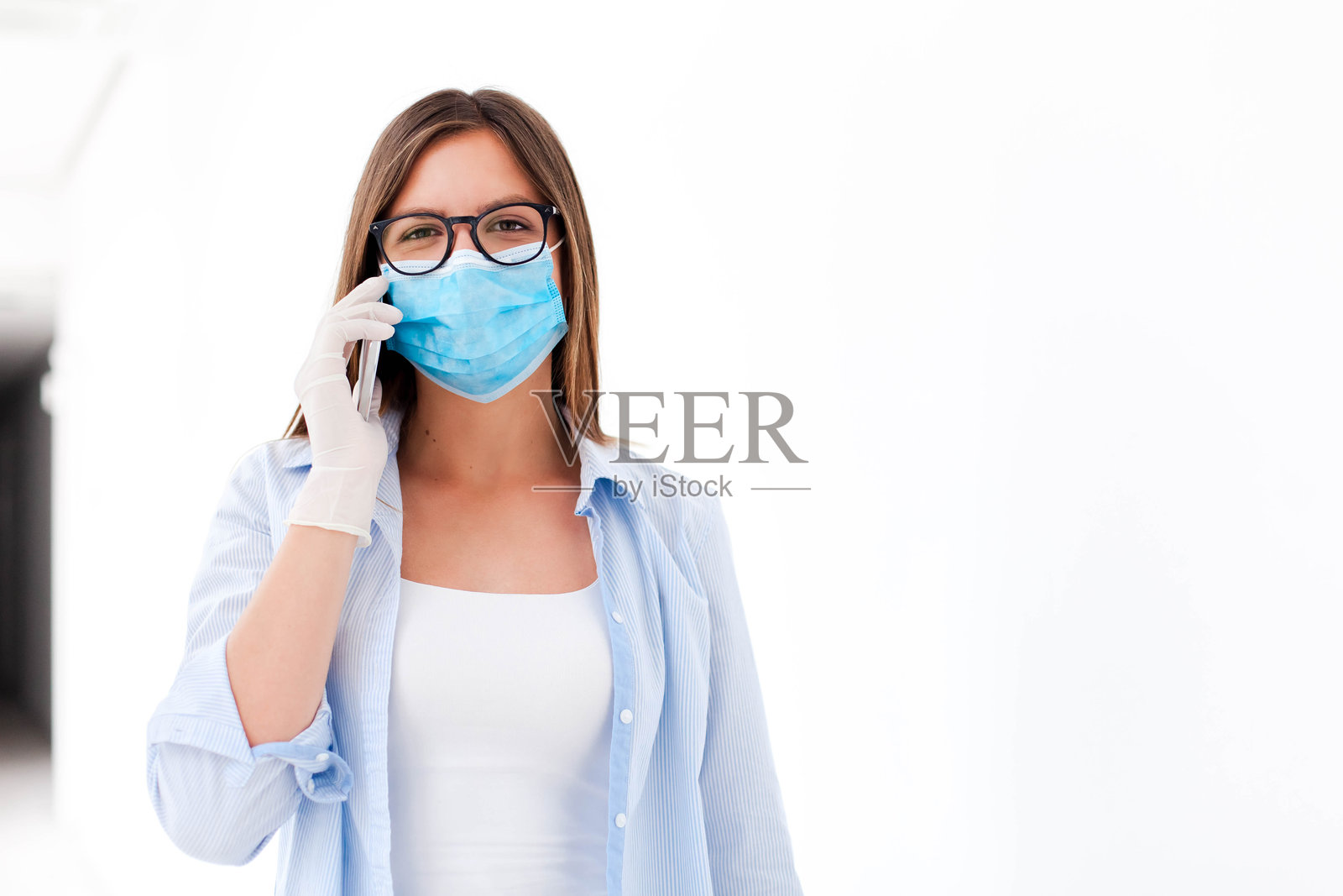 戴着口罩和医用手套的年轻女子。女孩在用手机打电话。穿着休闲服的工作人员照片摄影图片