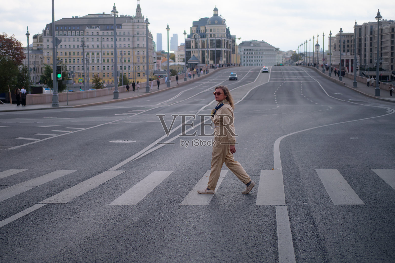 女人在城市人行横道上穿越马路，背景是莫斯科河大桥。都市生活场景，有女性行人。日常通勤与交通安全。一位中年妇女（50岁）。照片摄影图片