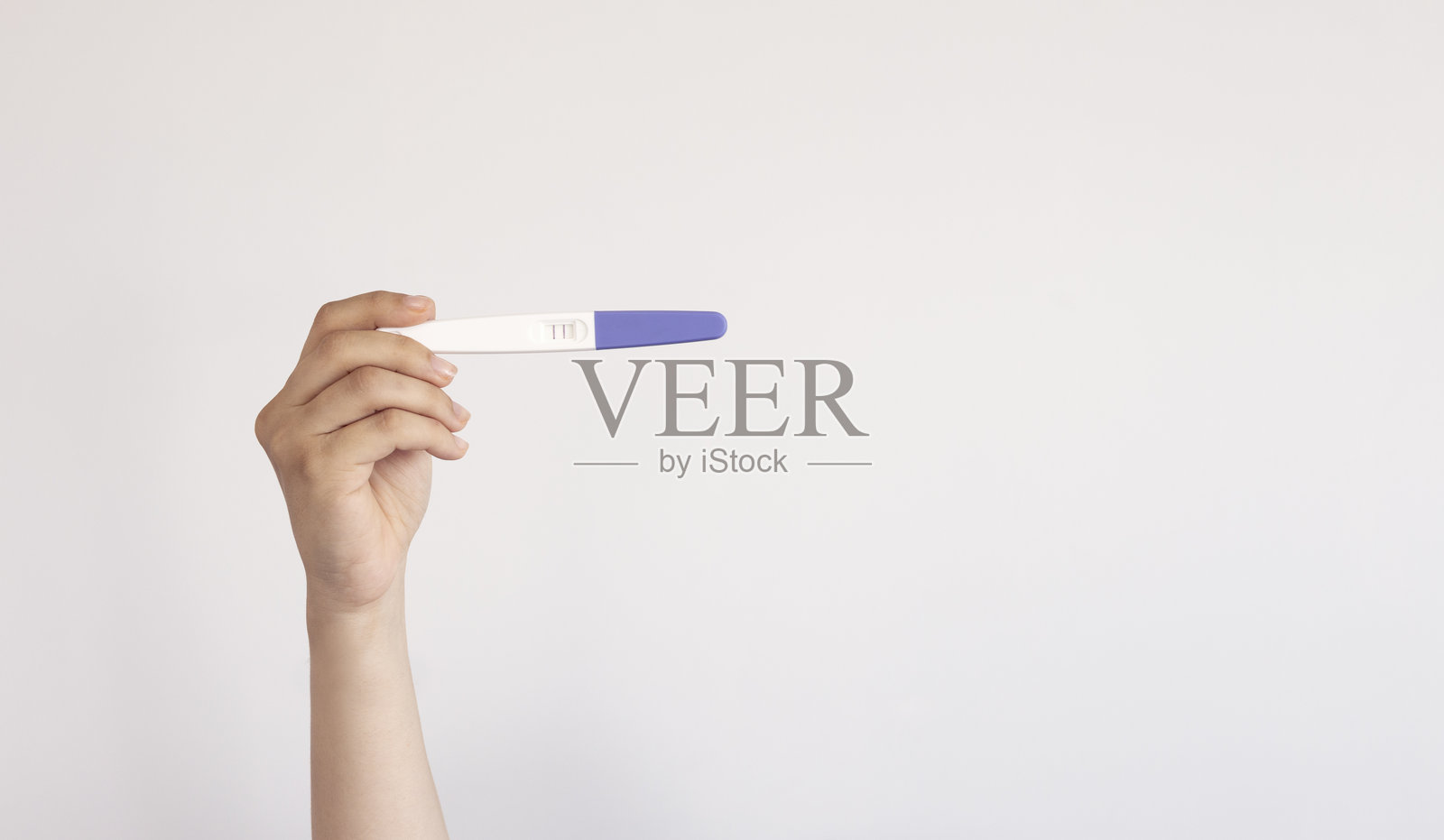 一名女子在灰色背景上拿着显示阳性结果的验孕棒，留有文字空间。照片摄影图片