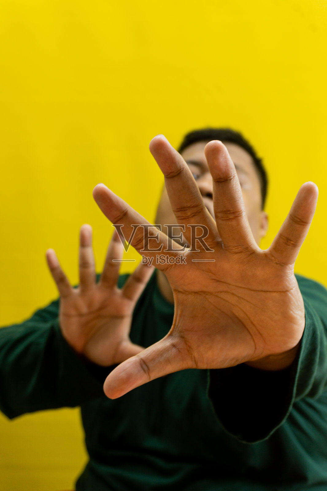 身穿长袖深绿色衬衫的男子张开手掌，手指张开，在黄色背景上，象征着警告、拒绝或通用的停止手势。照片摄影图片