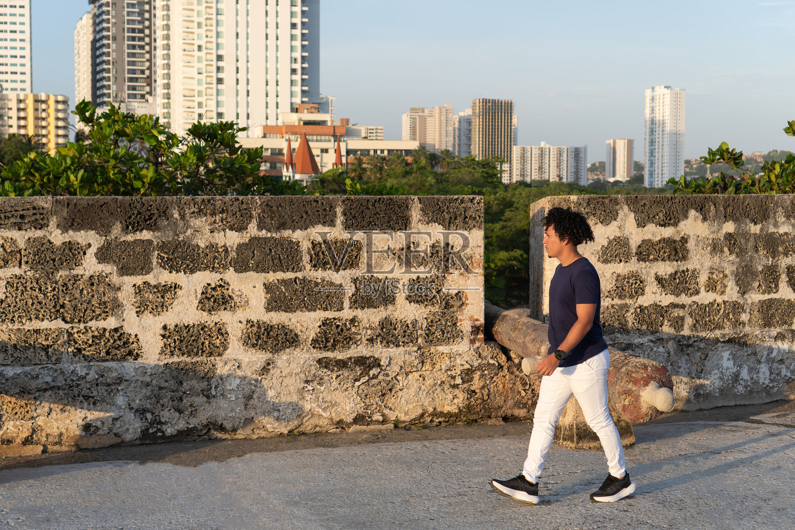 男人走在历史悠久的卡塔赫纳城墙上，背景是城市天际线。照片摄影图片
