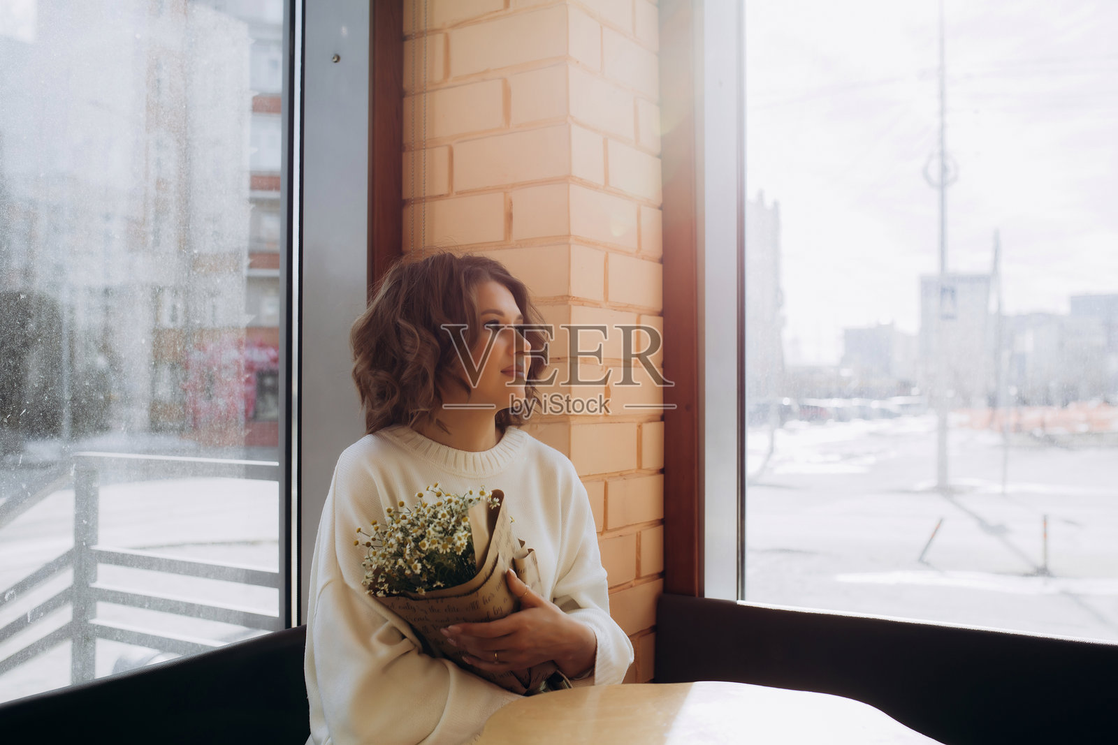 咖啡馆里，一位美丽的卷发女模特坐在桌前，桌上摆放着鲜花，画面为肖像式构图。照片摄影图片