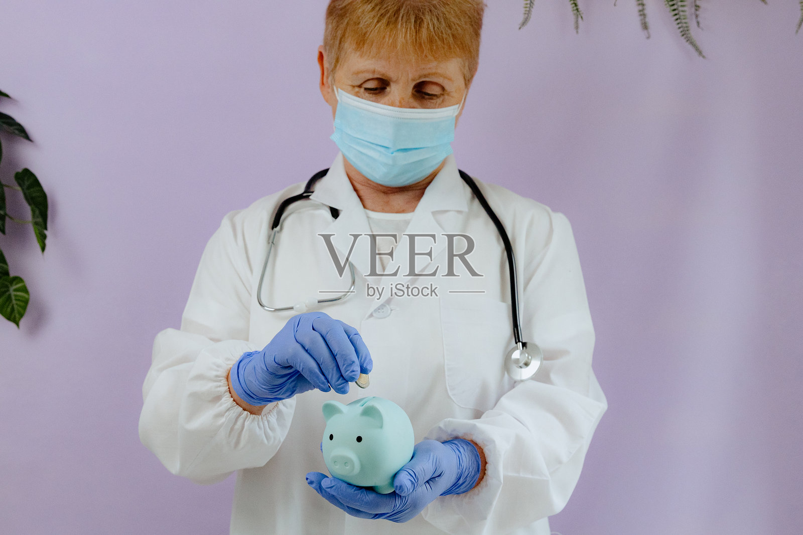 一位年长的医生手里拿着一个存钱罐，并往里投硬币。照片摄影图片