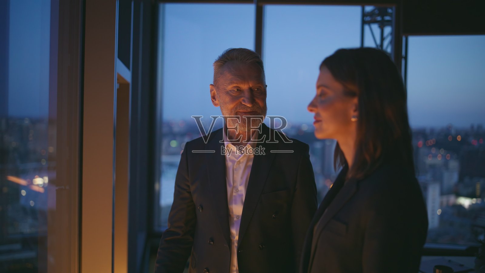 成功的同事在黑暗的工作室近景中，望着城市景观并握手。照片摄影图片