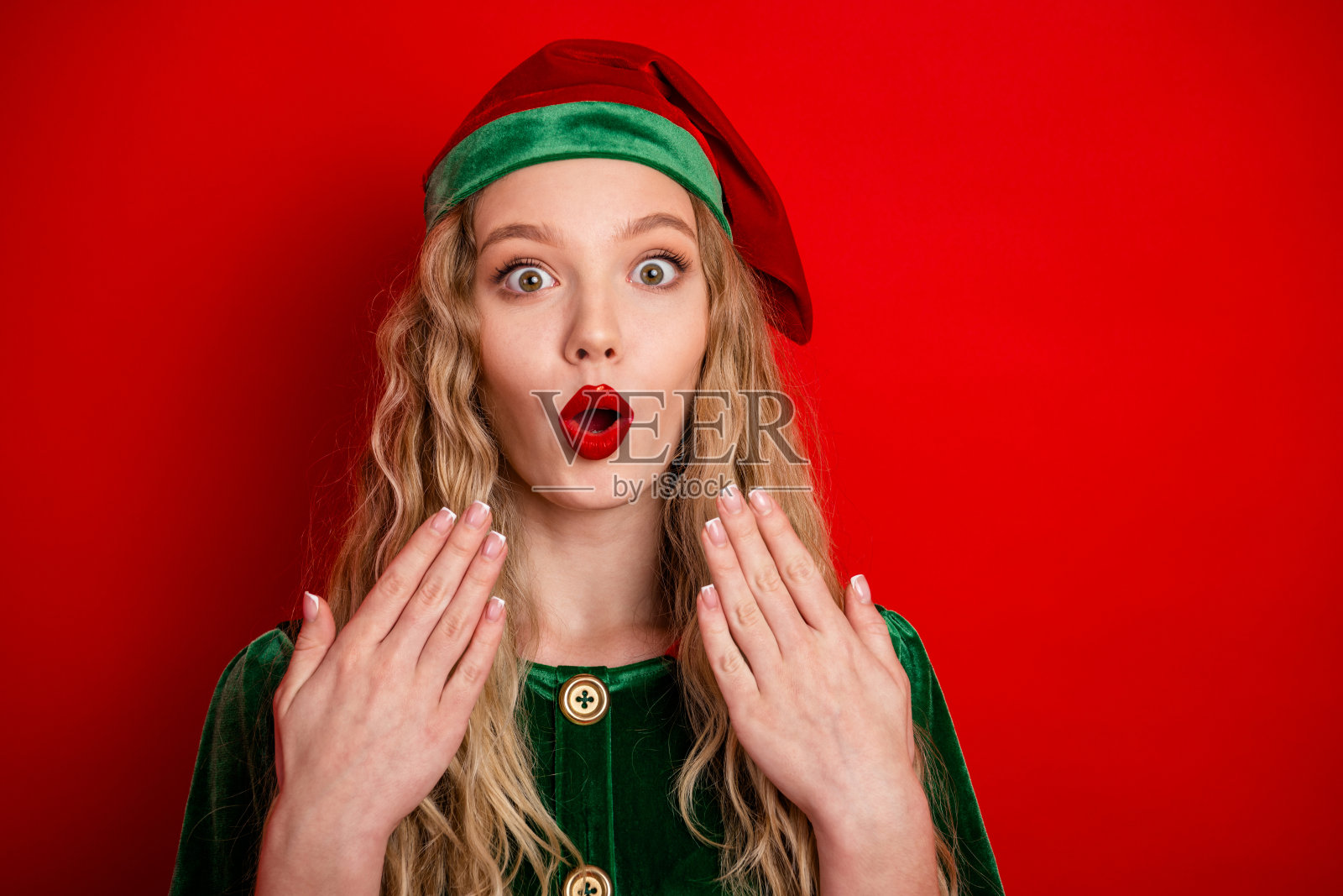 身着节日精灵服装的年轻女子，背景为亮红色，脸上洋溢着惊喜和节日的热情。照片摄影图片