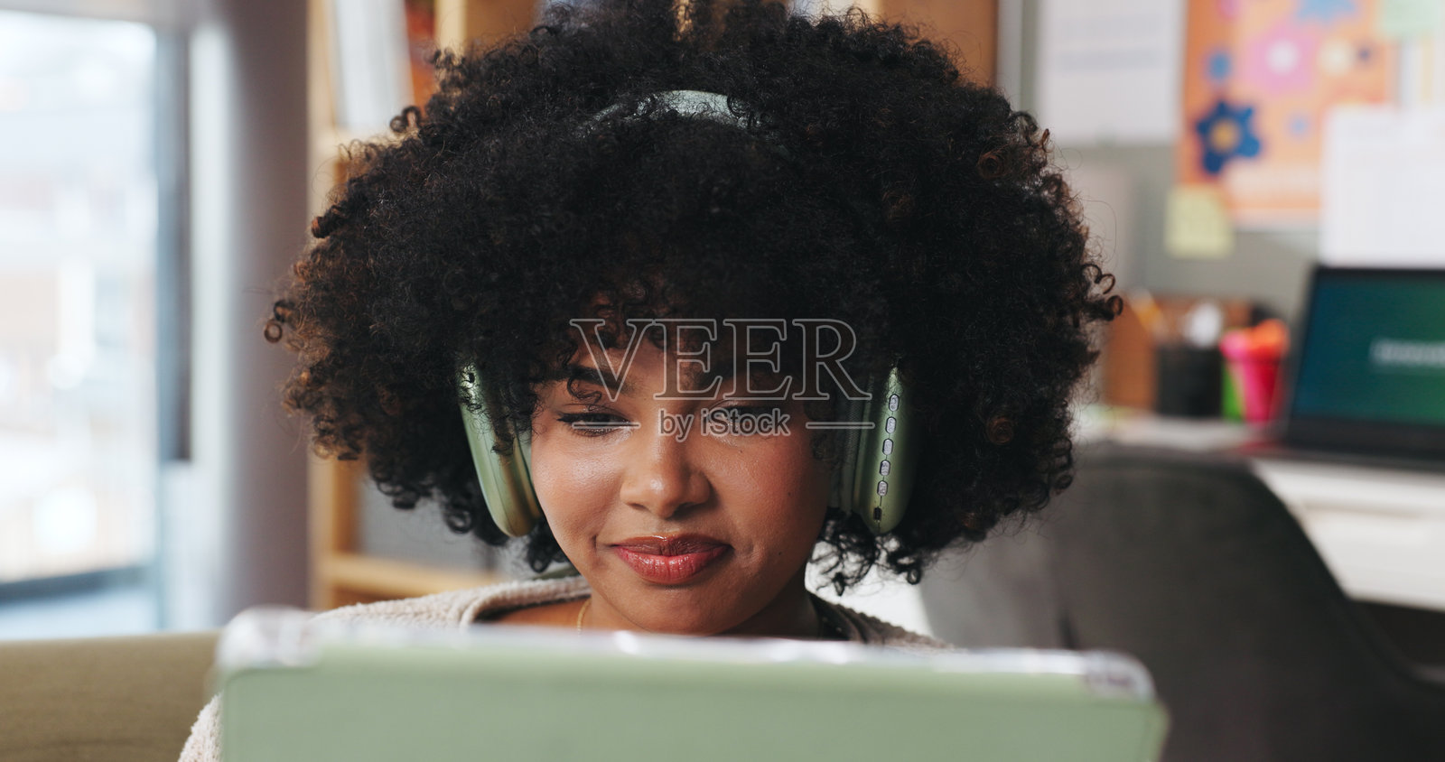 非洲女性，戴着耳机，在家中使用平板电脑进行流媒体播放、社交媒体和听音乐。快乐的女性，在沙发上放松地使用数码设备搜索电影、观看影片和收听播放列表。照片摄影图片