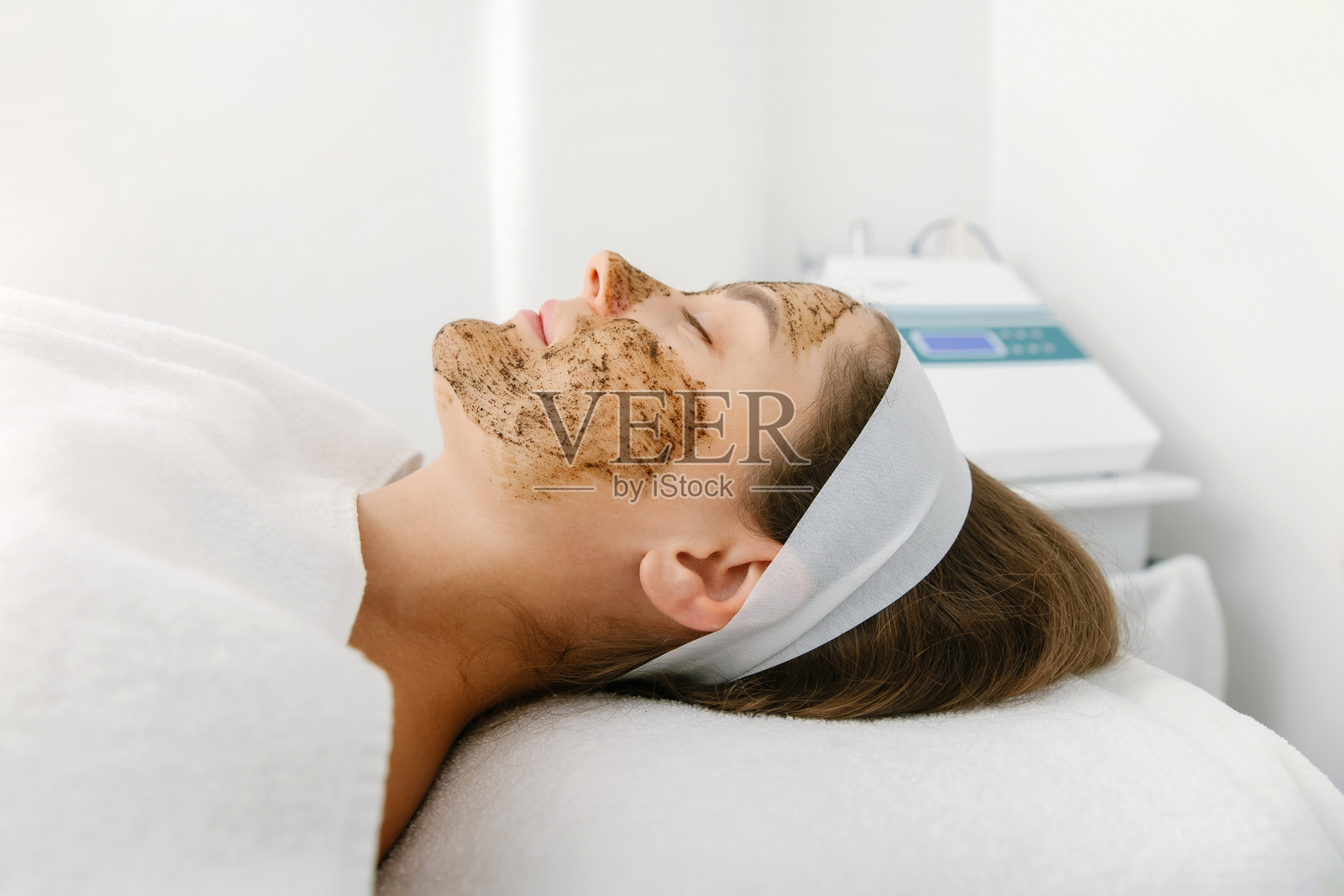 美容诊所的美容护理中，戴着头带的脸部泥膜放松水疗。照片摄影图片
