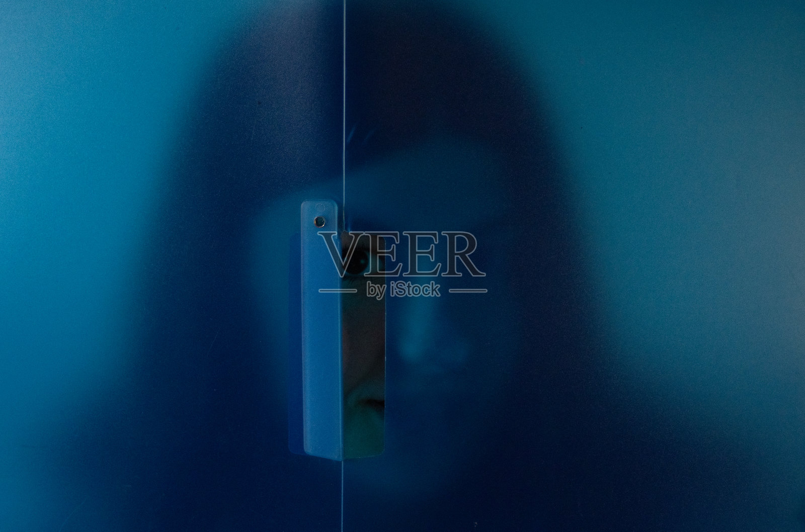 一位年轻女子从蓝色面板后面探出头来，非常适合创意宣传活动。照片摄影图片