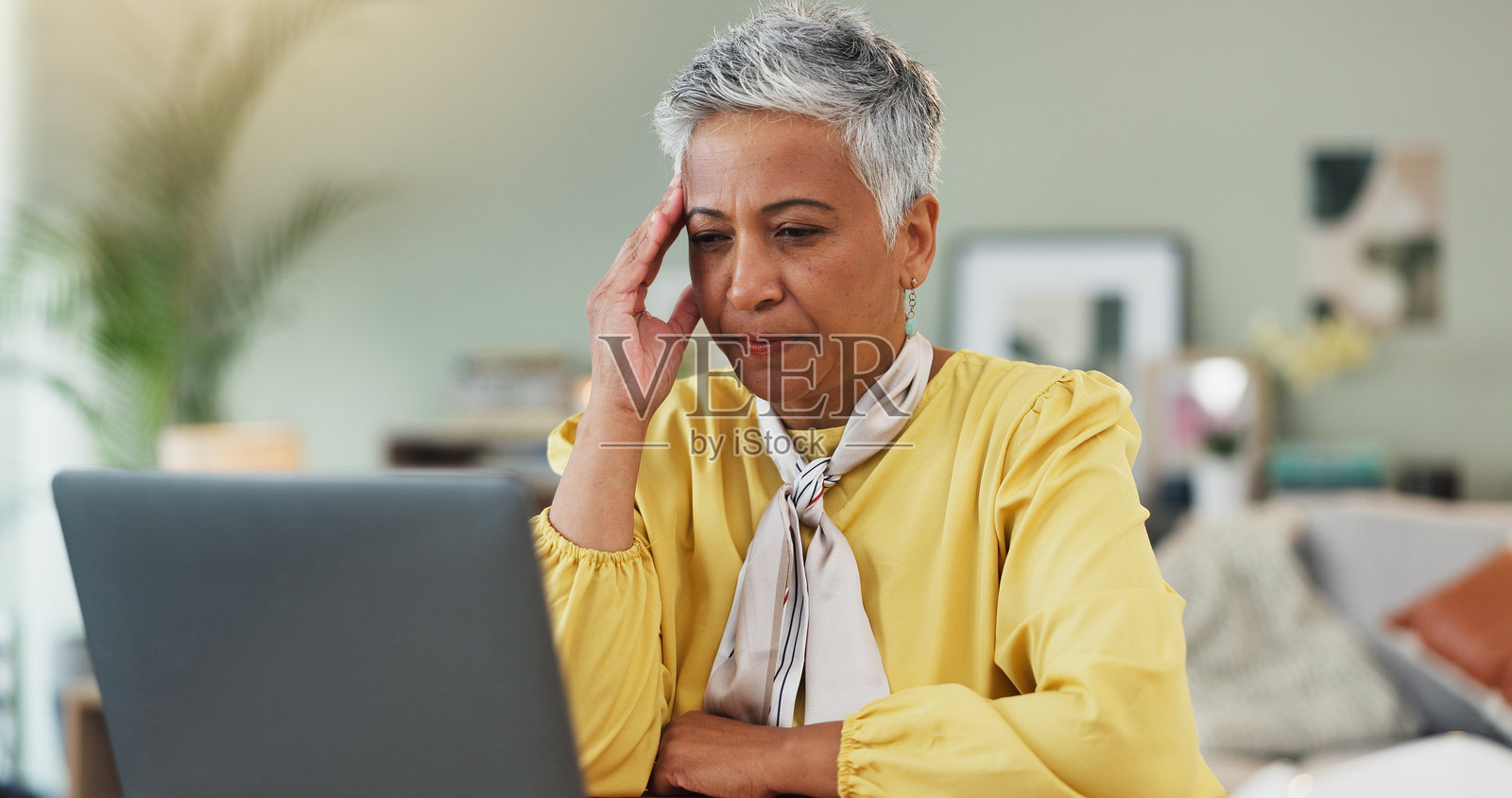 压力、头痛和在家使用笔记本电脑的成熟的女性，面临金融危机，正在思考退休生活。她感到沮丧，正在网上阅读账单、开支和银行贷款计划。照片摄影图片