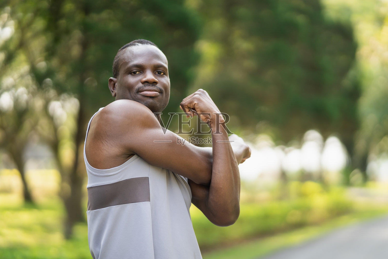 阳光明媚的日子里，一位自信的非裔美国男子在公园里展示肌肉，拥抱健身与力量，置身于自然环境中。照片摄影图片