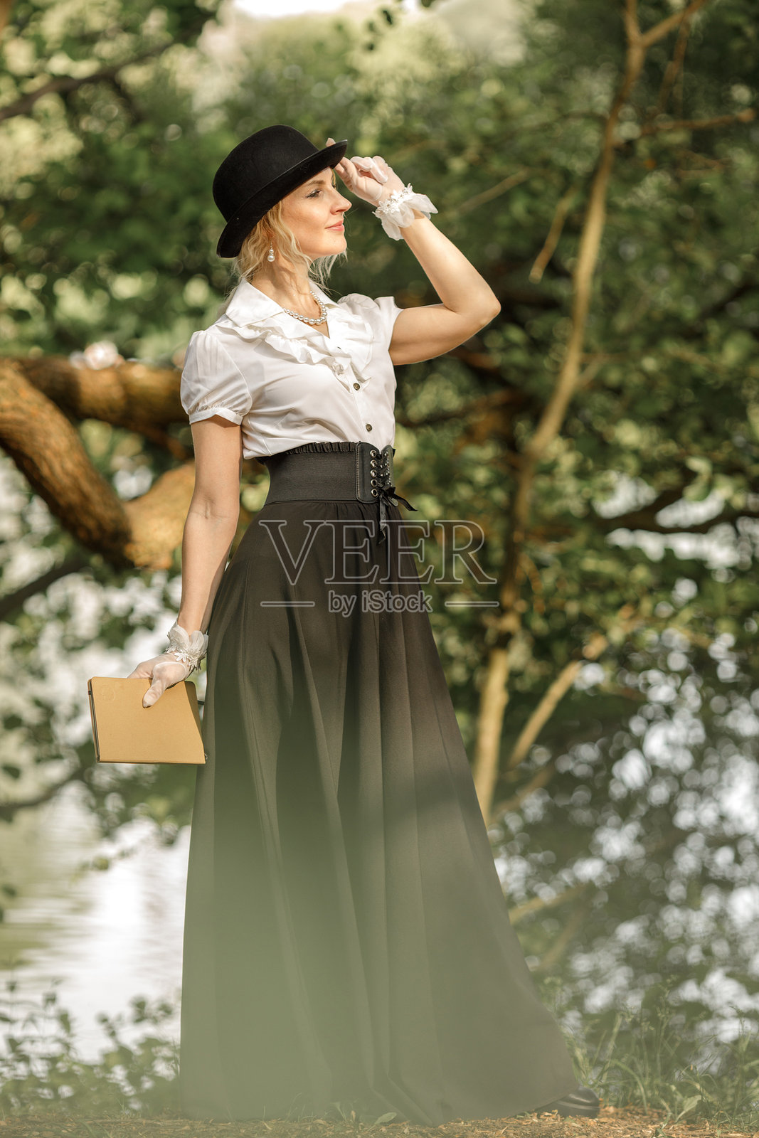 森林里，一位身着维多利亚时代服饰的金色长发美女手持书籍，复古风格。照片摄影图片