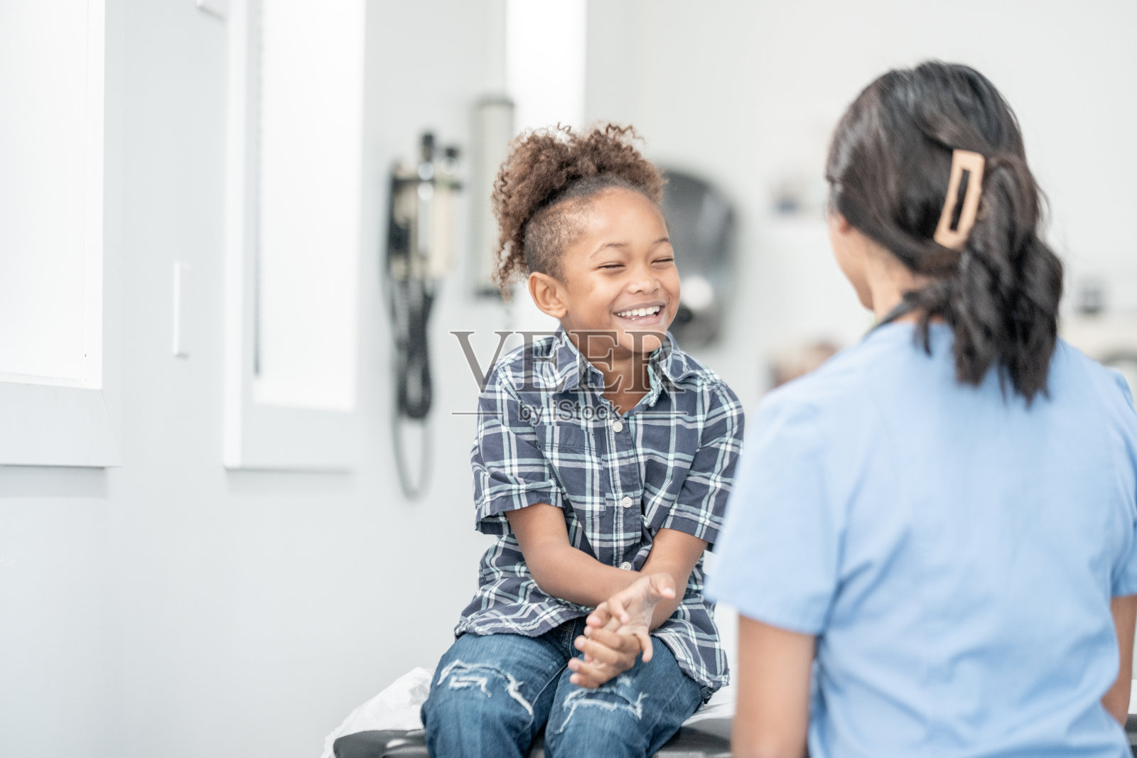 年轻快乐的黑人女孩在儿科诊所就诊时与女护士一起大笑照片摄影图片