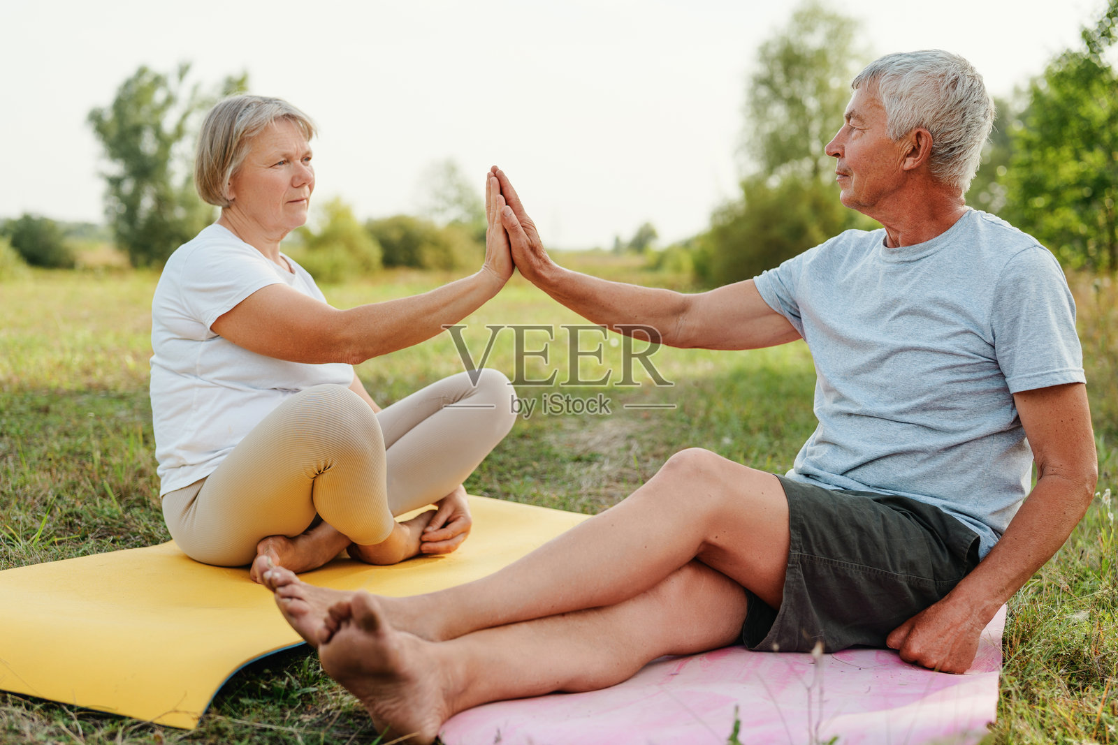 公园里，一对活跃的老年夫妇在瑜伽垫上击掌。照片摄影图片