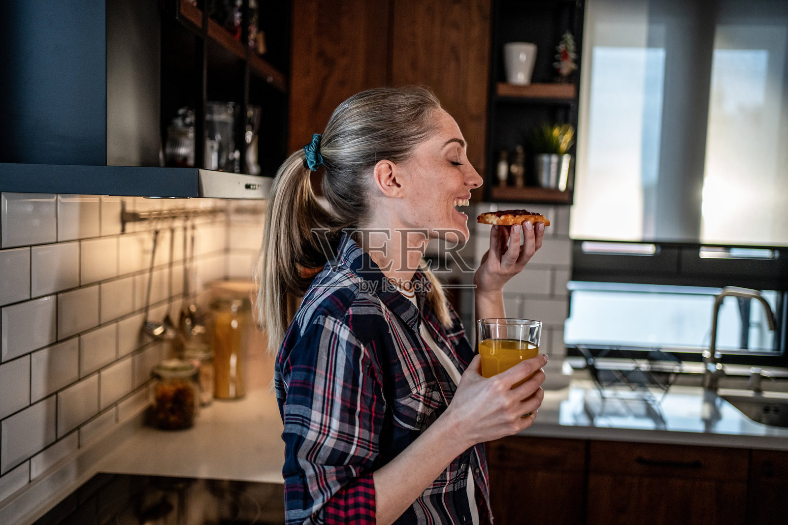 女人在厨房享用早餐，吃着吐司，喝着果汁照片摄影图片