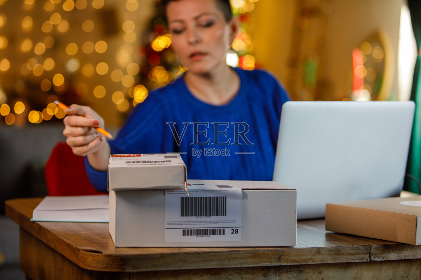 女人在节日季的家中办公室，在办公桌旁用笔记本电脑打包物品。照片摄影图片