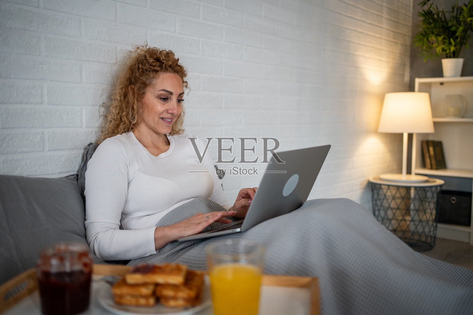 女人在床上用笔记本电脑工作，享用早餐照片摄影图片