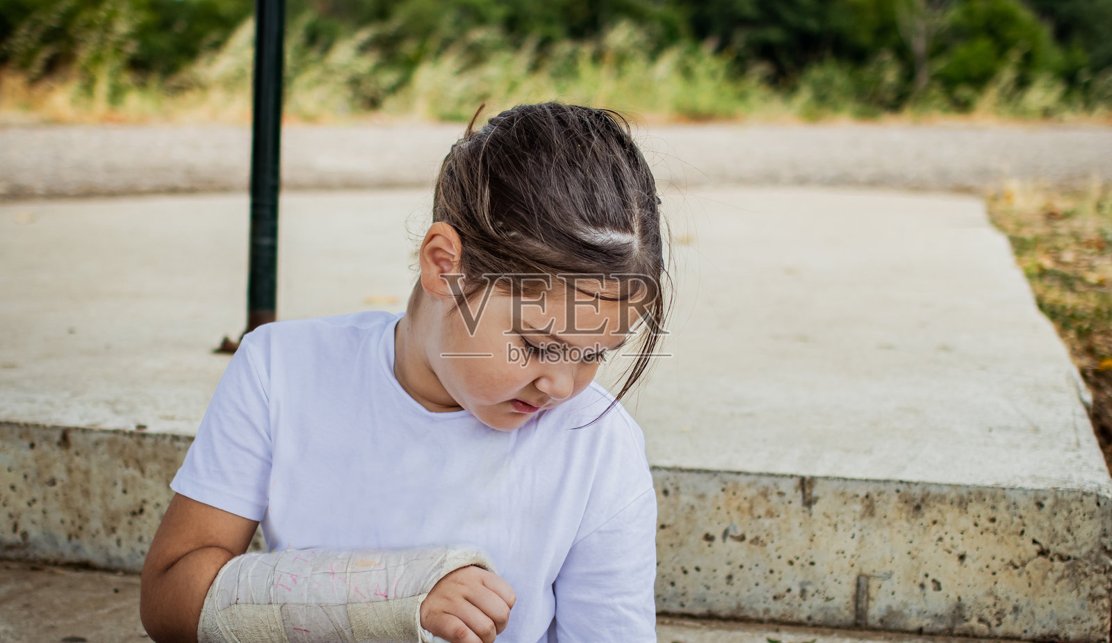 一个快乐、顽皮的小女孩，手臂打着石膏，在公园里享受活动的肖像。照片摄影图片