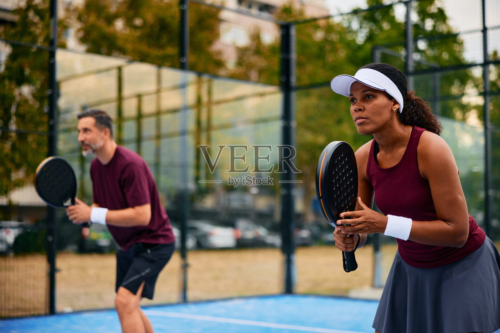 球场上，不同肤色的成年人手持球拍，准备打板式网球。照片摄影图片