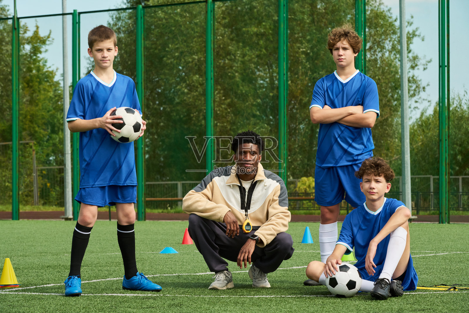 青少年男孩和黑人男性在训练期间于足球场上摆姿势照片摄影图片